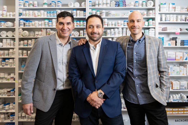 Mednow's three co-founders standing in front of pharmacy wall