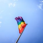LGBTQ flag blowing in the wind before a blue sky
