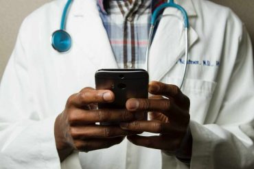 A doctor wearing a white coat holding a phone in their hands.