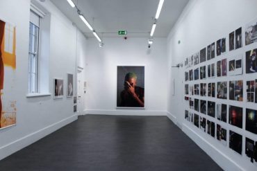 A room with white walls decorated with printed pictures. A photo of Frank Ocean is displayed in the center wall.