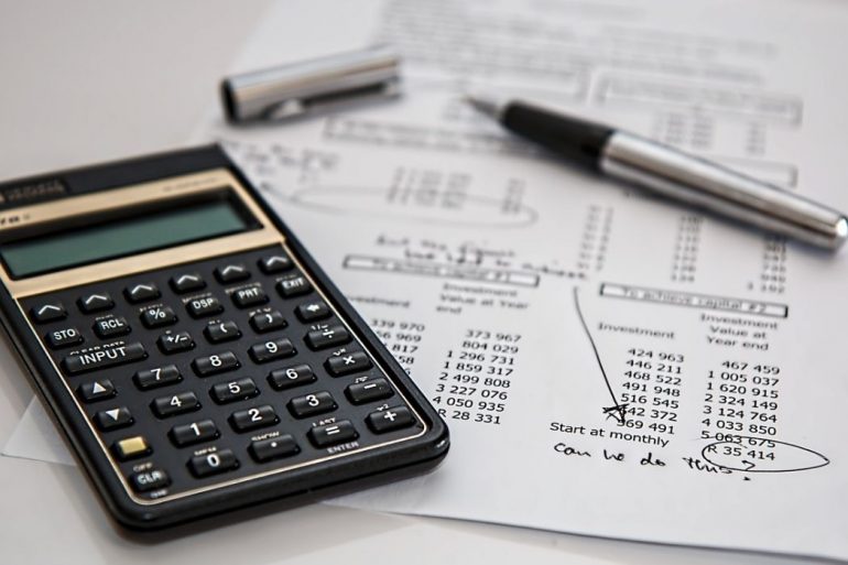 A black calculator and a sheet of white paper with financial statements on top of a white surface