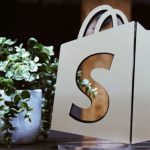 Shopify logo bag beside a green plant.