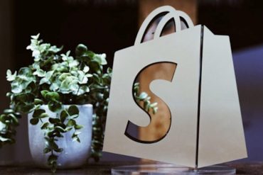 Shopify logo bag beside a green plant