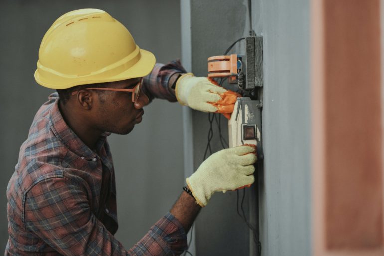 an electrician wearing a yellow helmet installs a switch on a wall in a commercial building