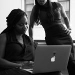 Black and white image of two women looking at a macbook.