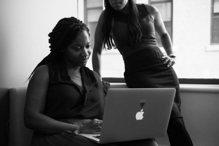 Black and white image of two women looking at a macbook