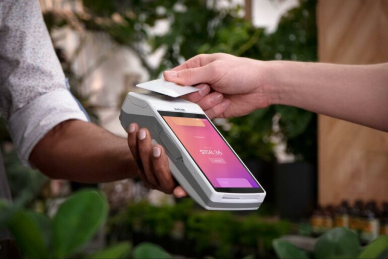 someone taps a payment card on a handheld terminal with a pink user interface on the screen