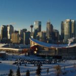 a view of calgary and the stadium from a high perch on a clear winter day with snow visible on the ground and a parking lot in the foreground