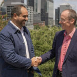 Cherif Habib, CEO of Dialogue, and Jacques Goulet, President of Sun Life, shake hands outdoors with the Montreal skyline in the background