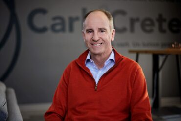 Jacob Homiller, newly-appointed CarbiCrete CEO is front and center. He is smiling. The CarbiCrete logo is on a wall in the background