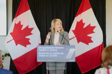 Melanie Joly stands at a podium in front of two Canadian flags