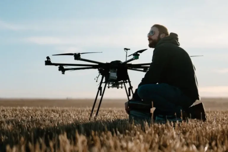 A man sits with a drone in a field