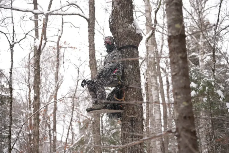 A hunter in camo wearing a Rozvelt mask while sitting in a tree