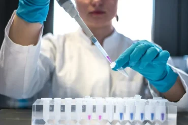 A researchers wearing gloves works with a pipet and small beakers.
