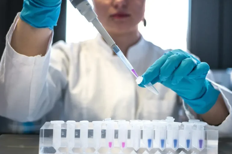 A researchers wearing gloves works with a pipet and small beakers.